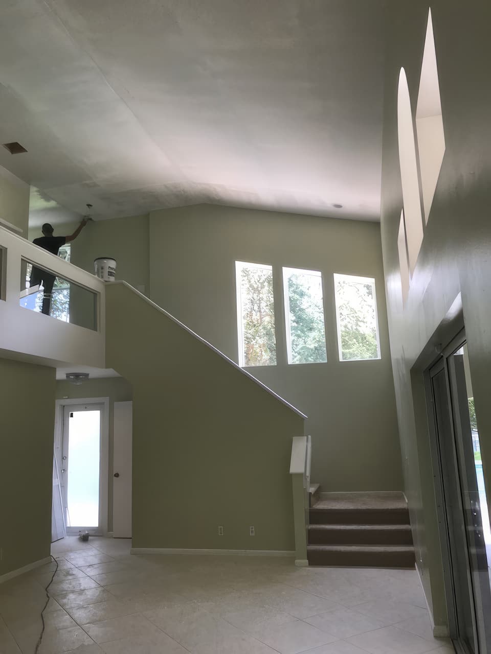 A two-story stair hall before the work: a closed stair behind a half wall, carpeted lower steps, green walls and a painter on the landing.