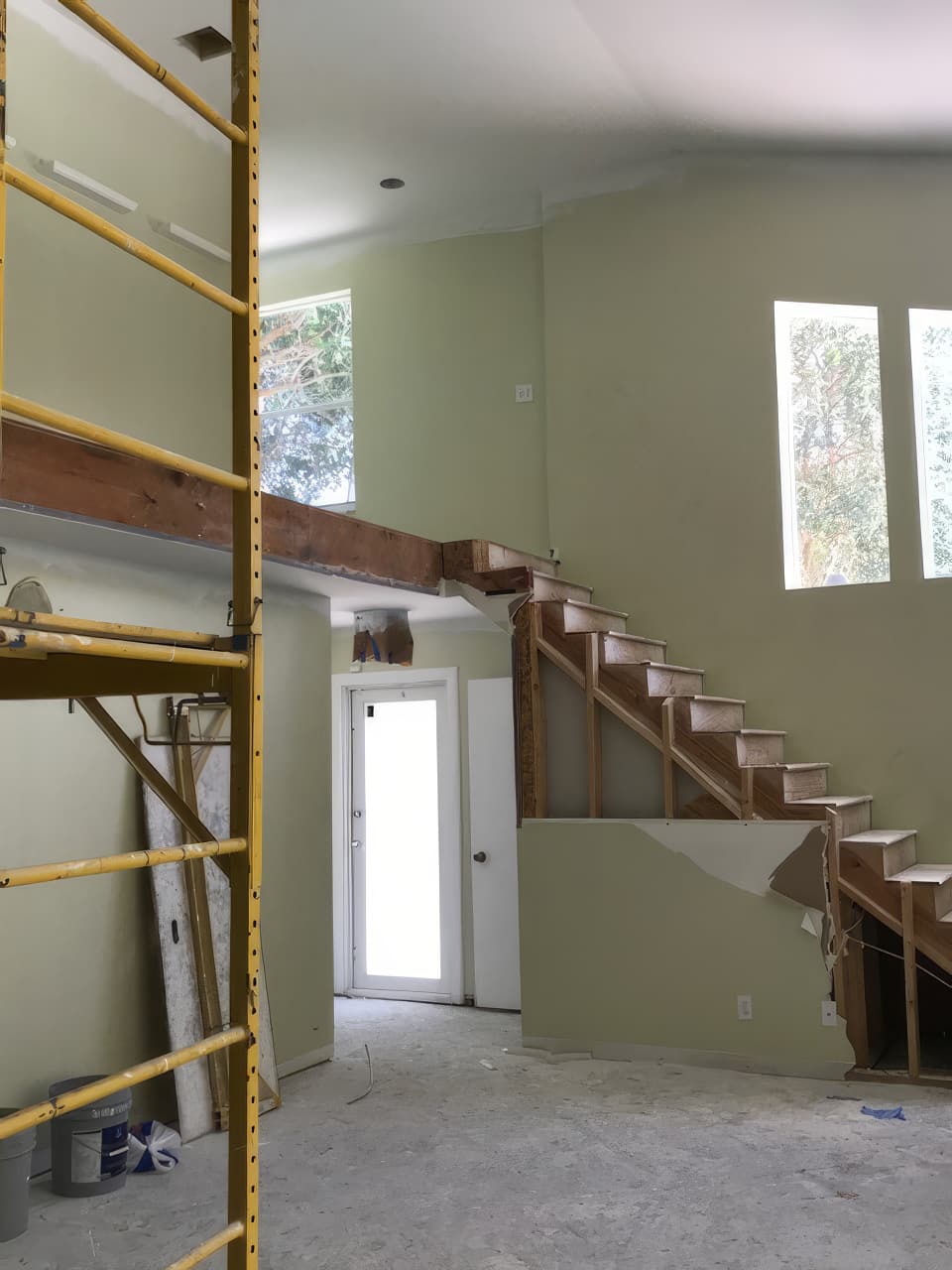 The same stair hall opened up: the half wall cut away to expose the wooden stair stringers, with yellow scaffolding in the hall.